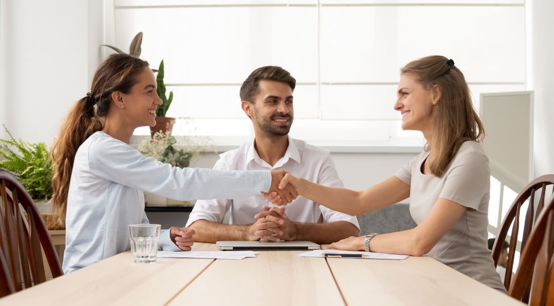 Three people sitting at a table. Two of them are shaking hands.